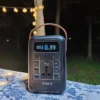 Portable power station on a table outdoors at night, with a glowing digital display and assorted outlets (USB, AC) visible, brown handle on top.